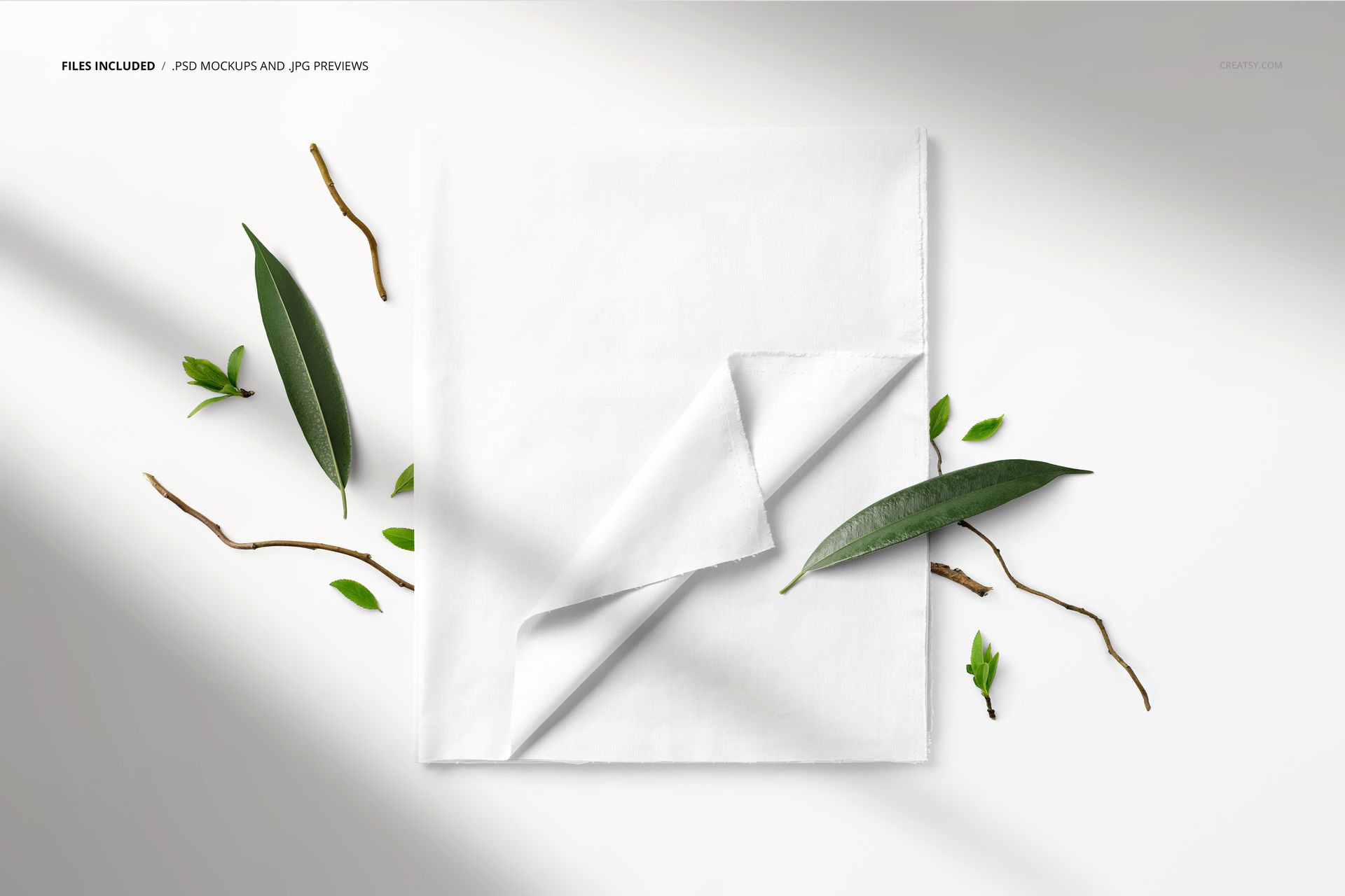 PSD mockup of a folded white textile surrounded by scattered green leaves and twigs, viewed from above.