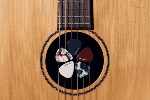 Top view of a wooden acoustic guitar featuring four uniquely designed guitar picks resting near the soundhole, mockup style.
