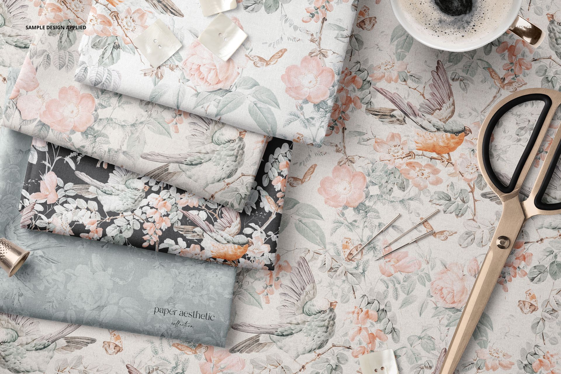 PSD mockup of several folded textiles in soft hues with nature-inspired prints, surrounded by scissors and pins on a tabletop.