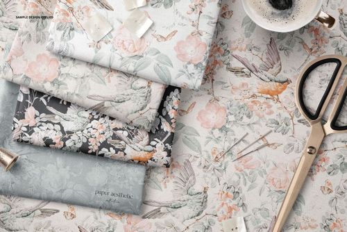 PSD mockup of several folded textiles in soft hues with nature-inspired prints, surrounded by scissors and pins on a tabletop.