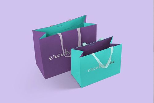 Mockup of two paper bags in different colors, featuring silver text and handles, placed side by side on a pastel background.