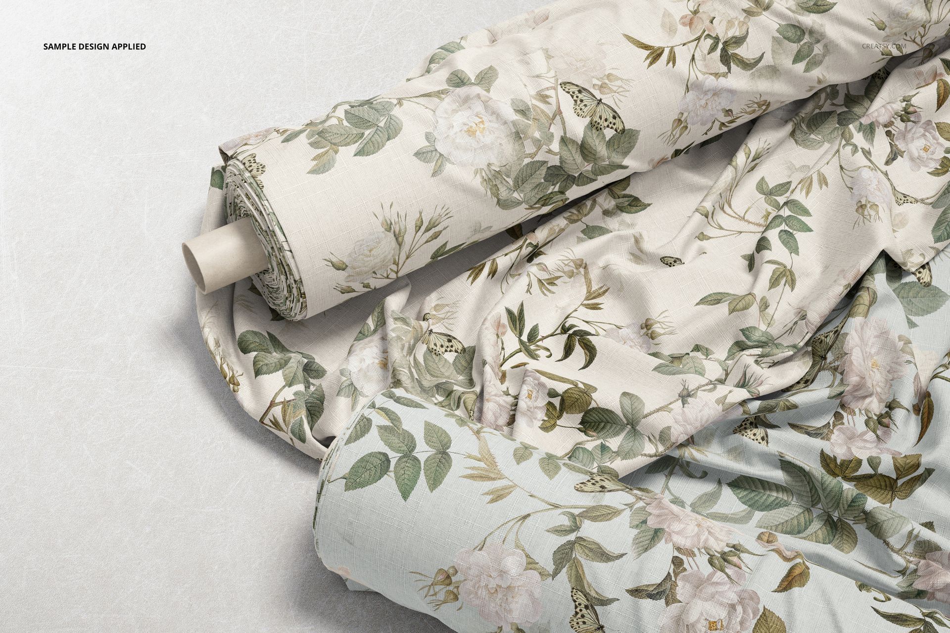 Fabric rolls with floral and leafy patterns in muted green and beige tones, viewed from above on a light surface.