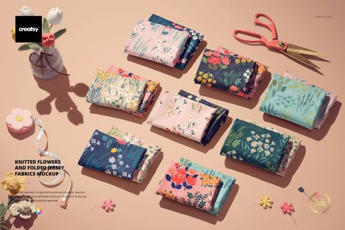 PSD mockup showing multiple folded fabric pieces with vibrant flower motifs, surrounded by crafting props on a light tabletop.
