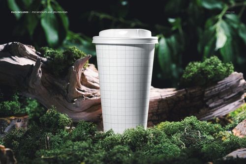 PSD mockup of a paper cup featuring a blank grid design, placed among green moss and tree bark in a forest.