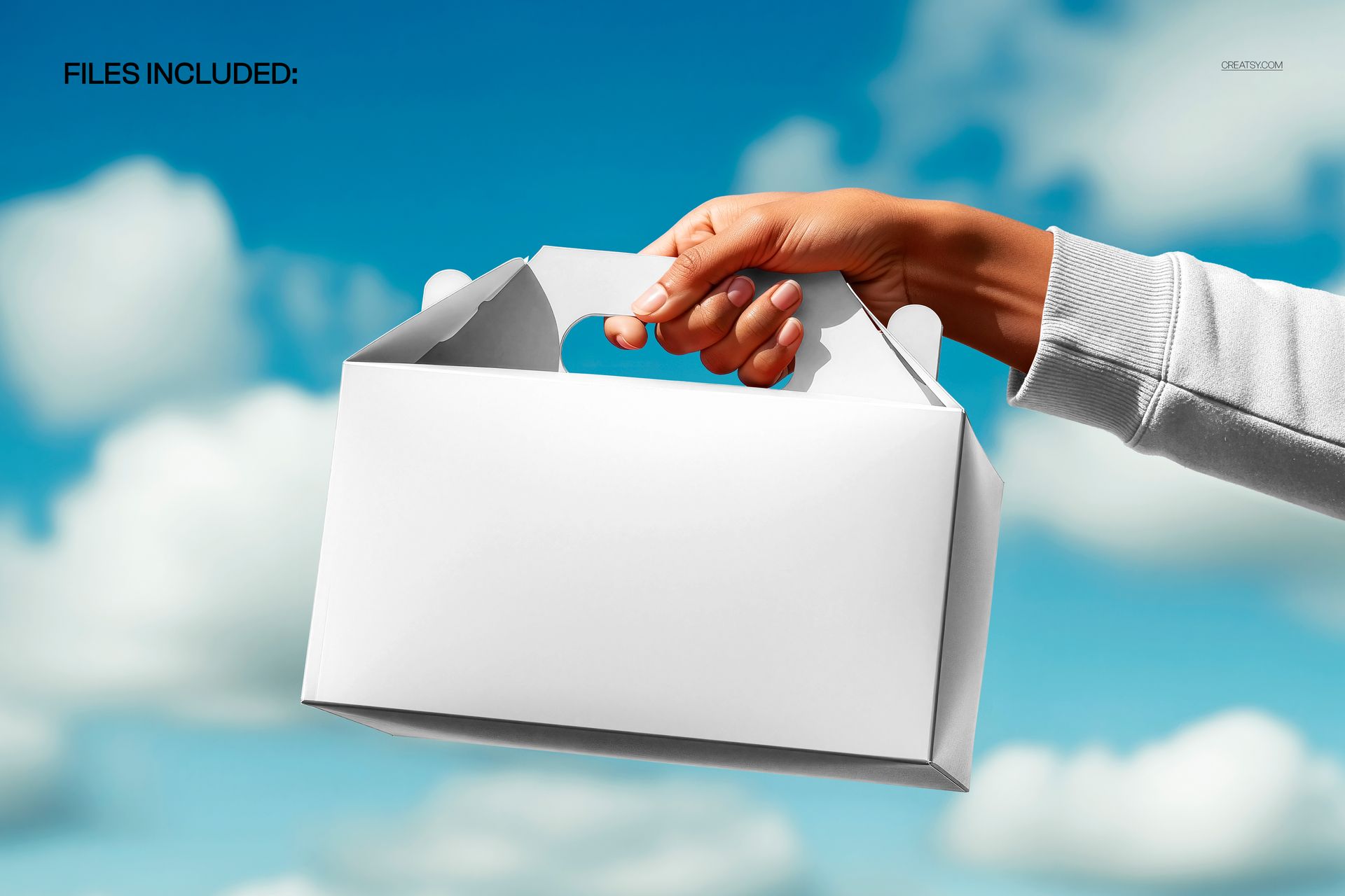 White packaging gable box mockup held in one hand, sky and clouds visible in the background.