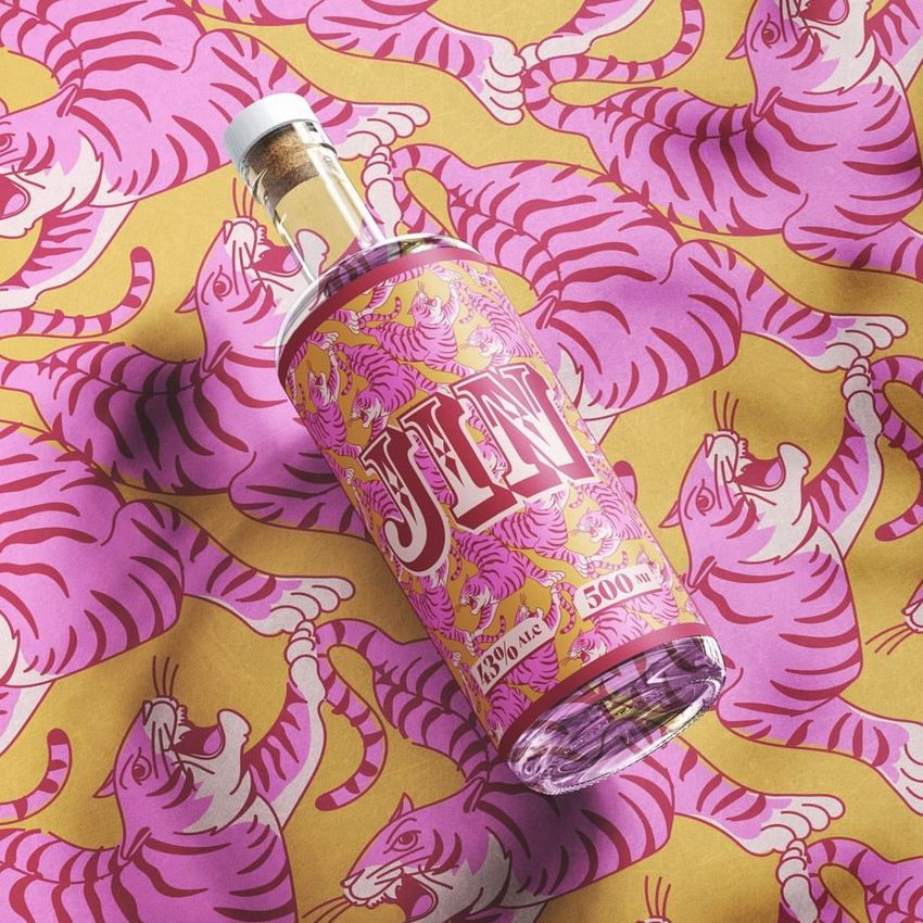 Glass bottle mockup with a cork top, featuring a pink and yellow tiger pattern label, placed on matching patterned fabric.