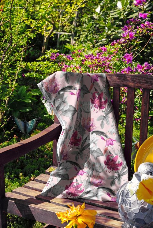 PSD mockup showing a botanical print fabric casually placed on a wooden bench amid blooming garden scenery.