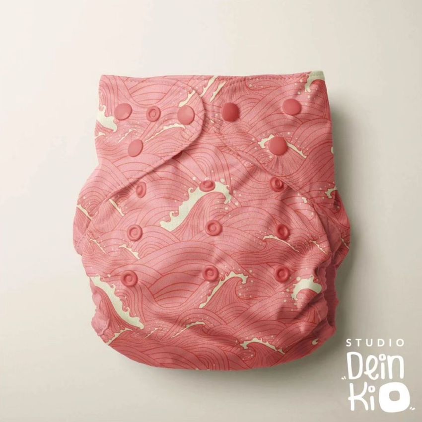 Reusable baby cloth diaper mockup featuring a pink ocean wave pattern, photographed from above on a light background.