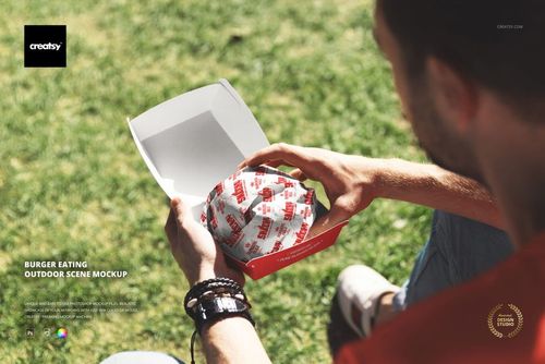 Outdoor PSD mockup showing a wrapped burger in a red box held by a person, with grass visible in the background.