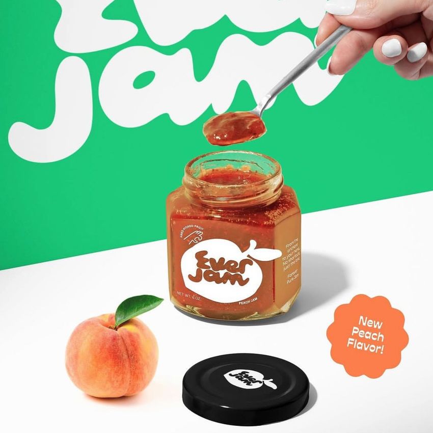 Apricot jam jar mockup with a spoon lifting jam, a whole peach, and a black lid on a white surface with a green background.