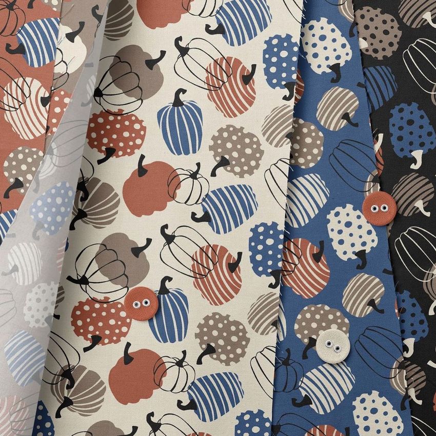 Fanned cotton fabric mockup displaying several stacked swatches with pumpkin patterns in beige, blue, rust, and black tones.