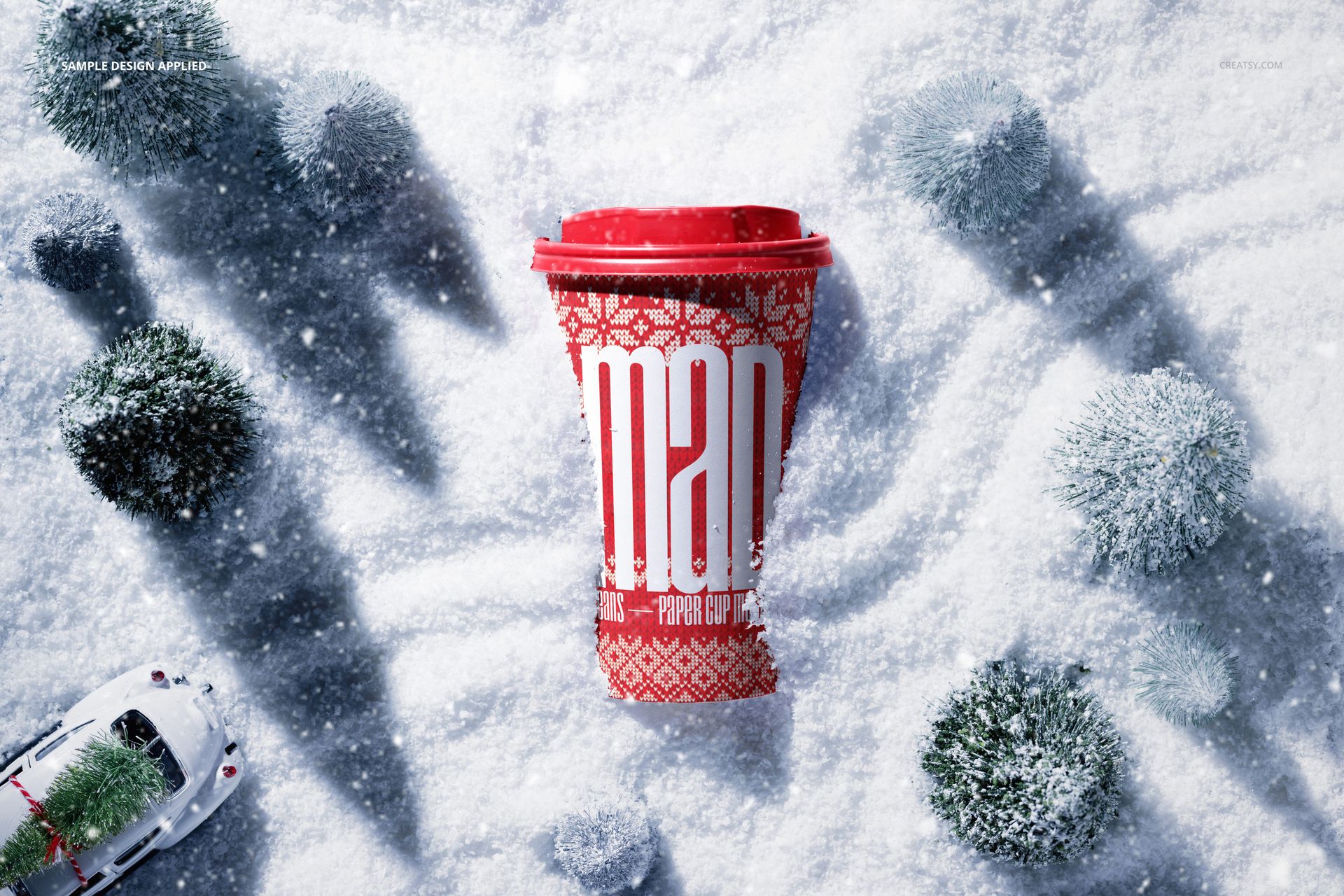 Red paper coffee cup mockup with holiday design, surrounded by snow and miniature trees, viewed from above.