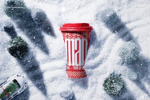 Red paper coffee cup mockup with holiday design, surrounded by snow and miniature trees, viewed from above.