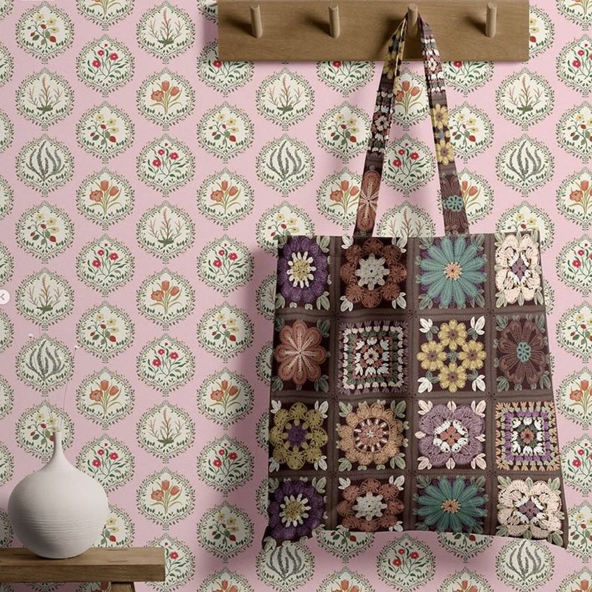 Tote bag mockup featuring a crochet-patterned bag hanging on a wooden wall hook, set against a pink floral wallpaper.