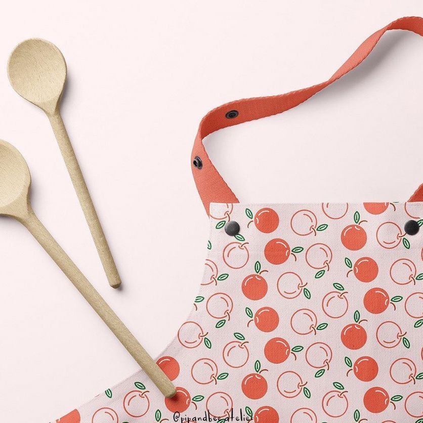 Kids apron mockup featuring a peach pattern, shown from above on a light pink surface with two wooden spoons beside it.