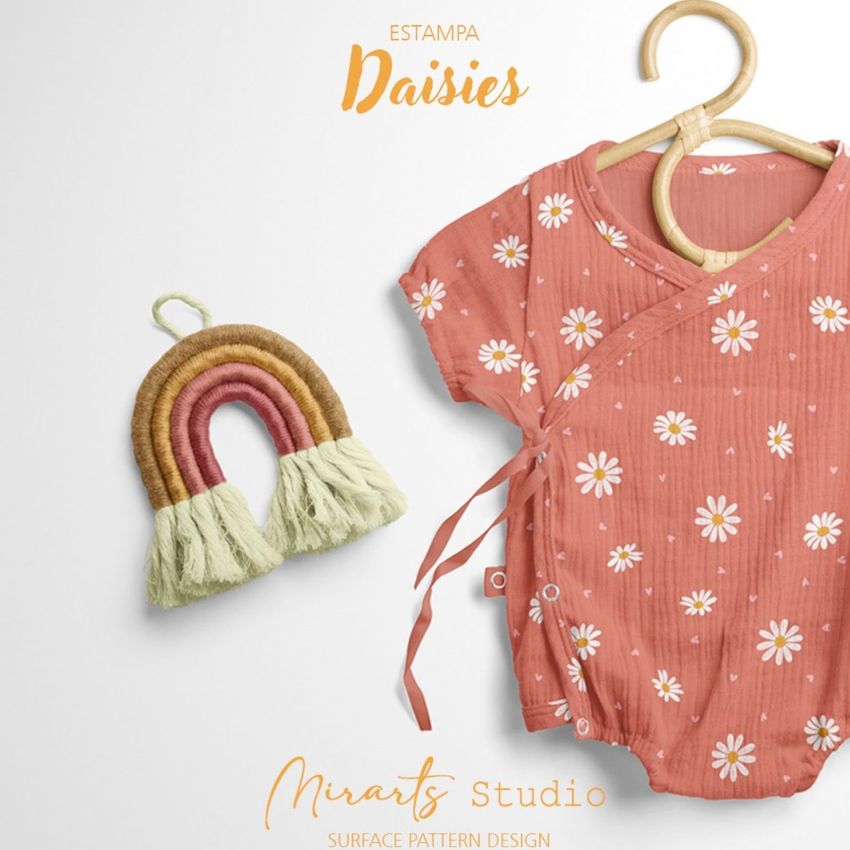Muslin onesie mockup featuring a short-sleeve baby romper with a daisy pattern, displayed on a wooden hanger next to a woven rainbow decor.