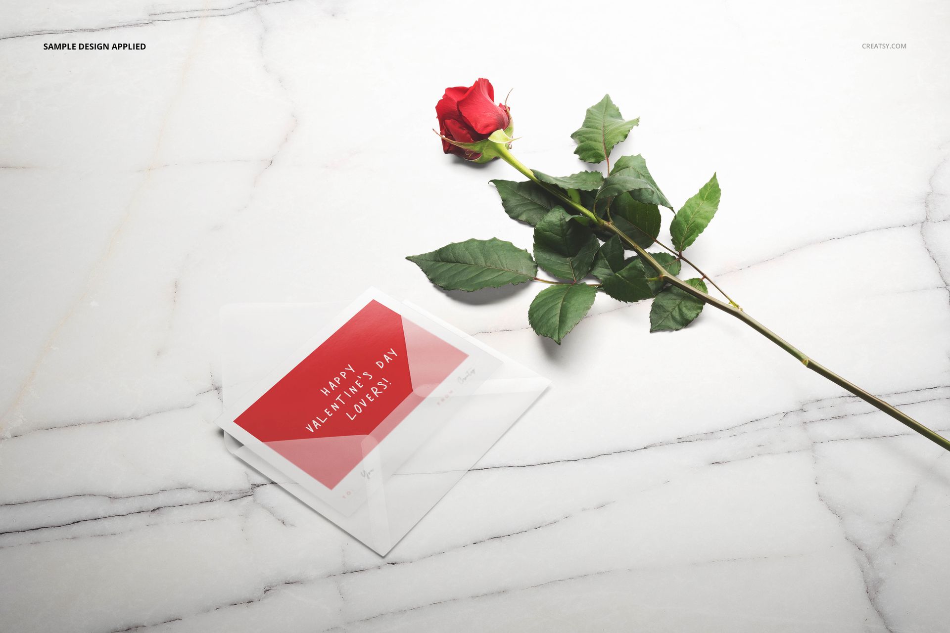 Valentine’s stationery mockup featuring a transparent envelope with a red card and a fresh red rose on marble.