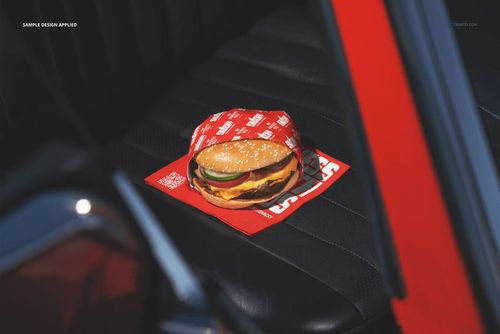 PSD mockup featuring a hamburger in red packaging placed on a dark car seat, with sunlight highlighting the scene.