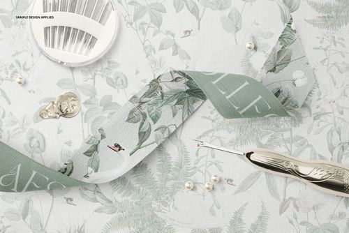 Wide cotton ribbon mockup featuring leafy green design, sewing needle case, pearls, and crochet hook on patterned cloth.