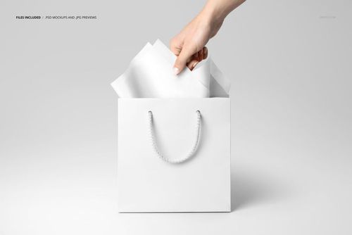 Square white paper bag with rope handles holding white tissue paper, hand visible from above, shown in PSD mockup.