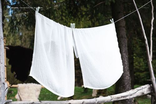 Two white muslin cloths draped on a line outdoors, surrounded by green forest and wooden branches, PSD mockup scene.