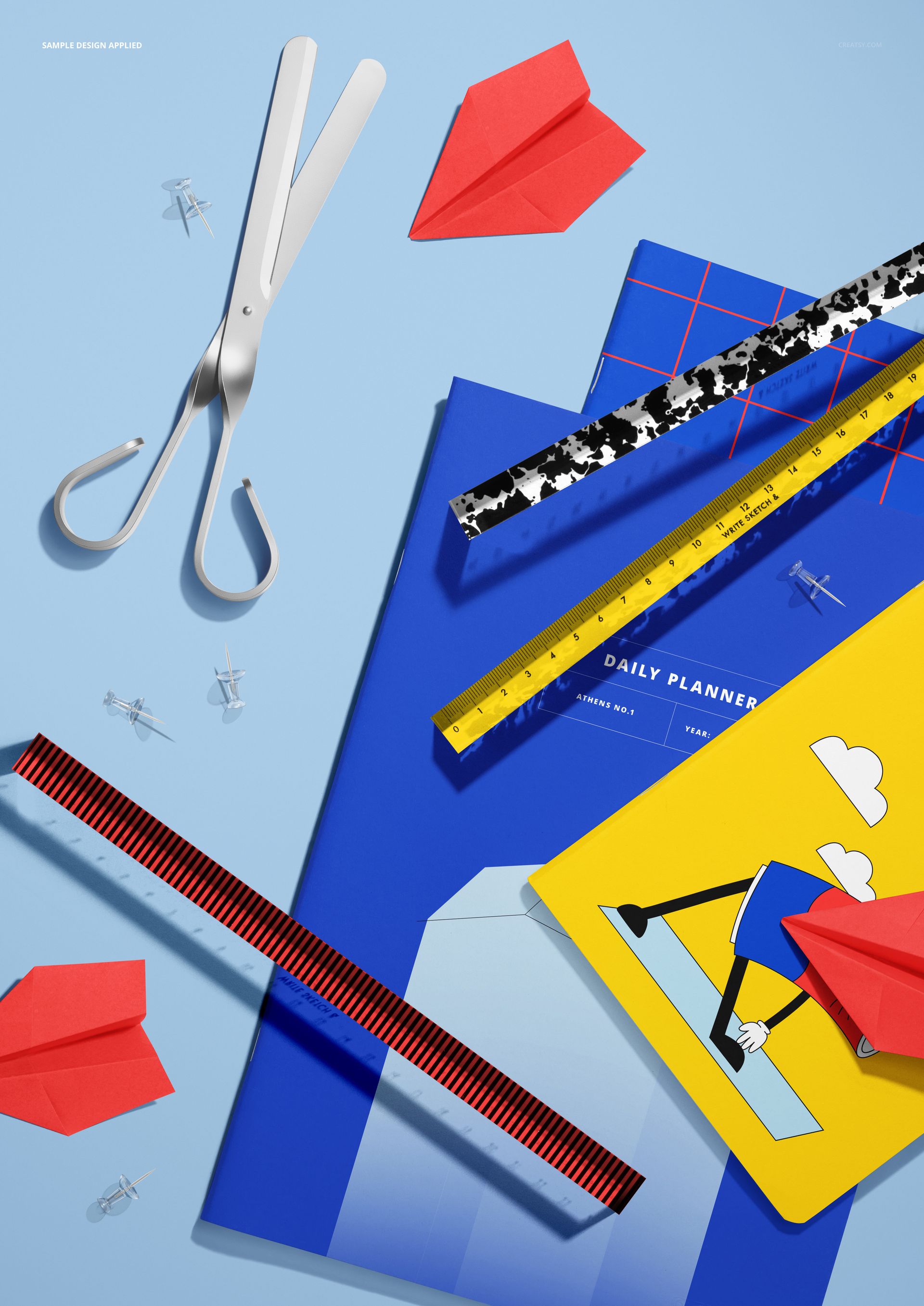 PSD mockup featuring school notebooks, rulers, scissors, and paper planes displayed on a light blue tabletop.