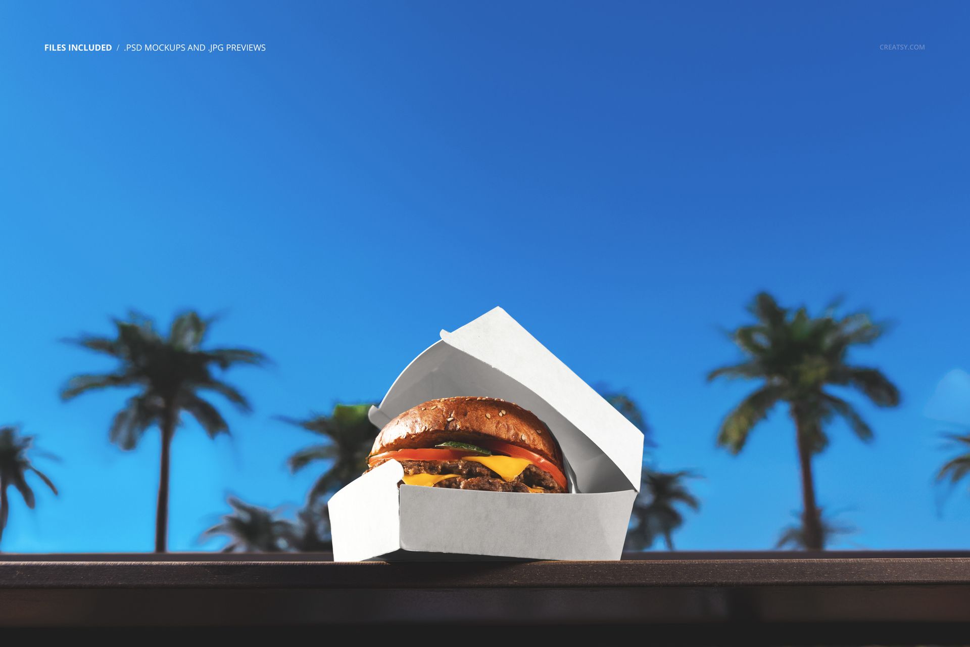 Front view of a white burger box mockup displaying a burger, set outdoors against blurred palm trees and bright sky.