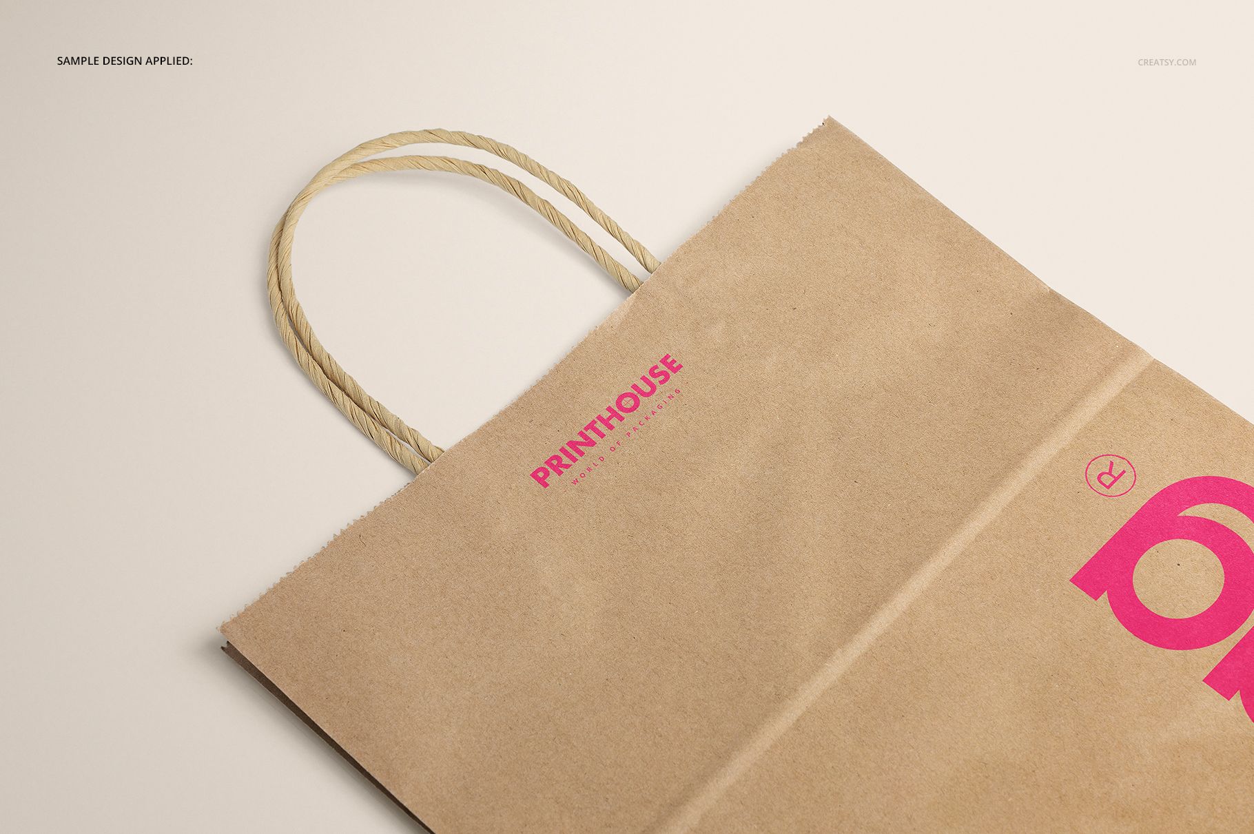 Mockup of a brown kraft paper shopping bag featuring rope handles and pink printed text, displayed in partial view.