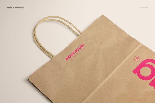 Mockup of a brown kraft paper shopping bag featuring rope handles and pink printed text, displayed in partial view.