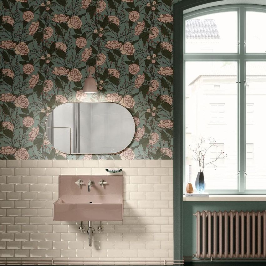Vintage bathroom mockup featuring a pink sink, oval mirror, and floral wallpaper above white subway tiles near a large window.