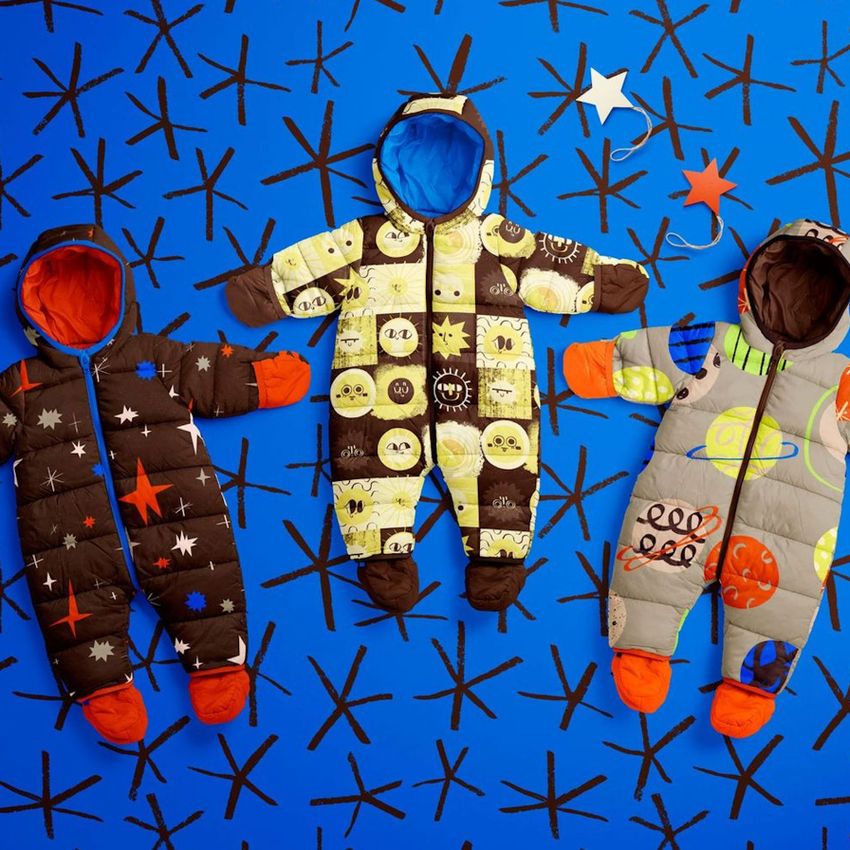 Assorted baby snowsuit mockups with orange feet and space-inspired prints displayed flat on a blue surface with star motifs.