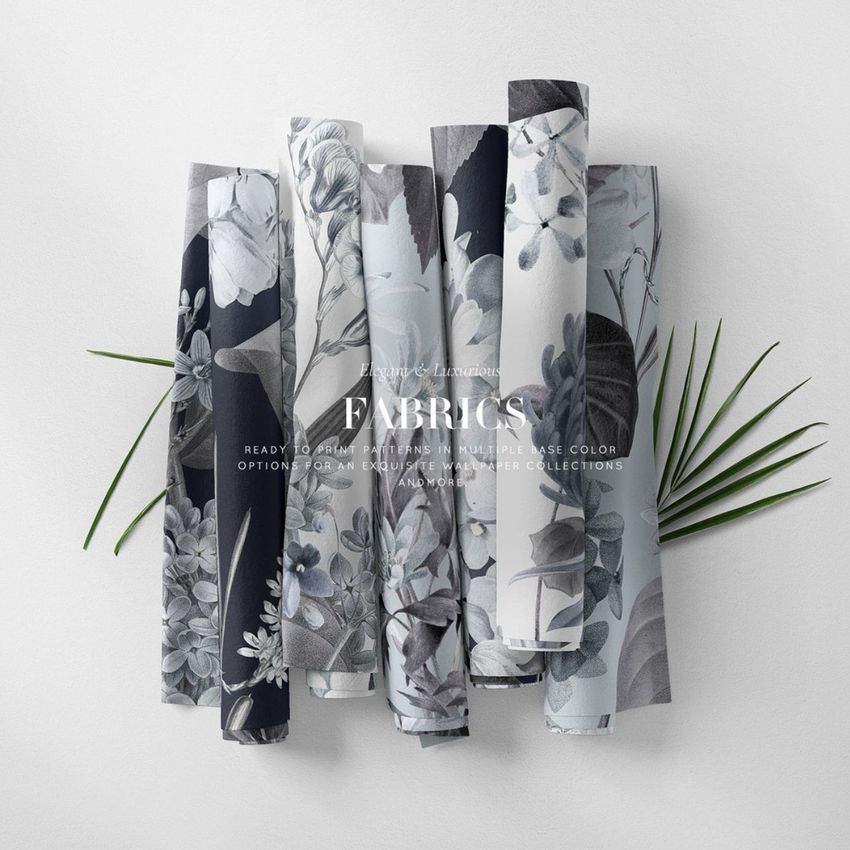 Fabric rolls mockup featuring several rolls with elegant floral patterns in shades of gray and blue, arranged on a white surface with palm leaves.