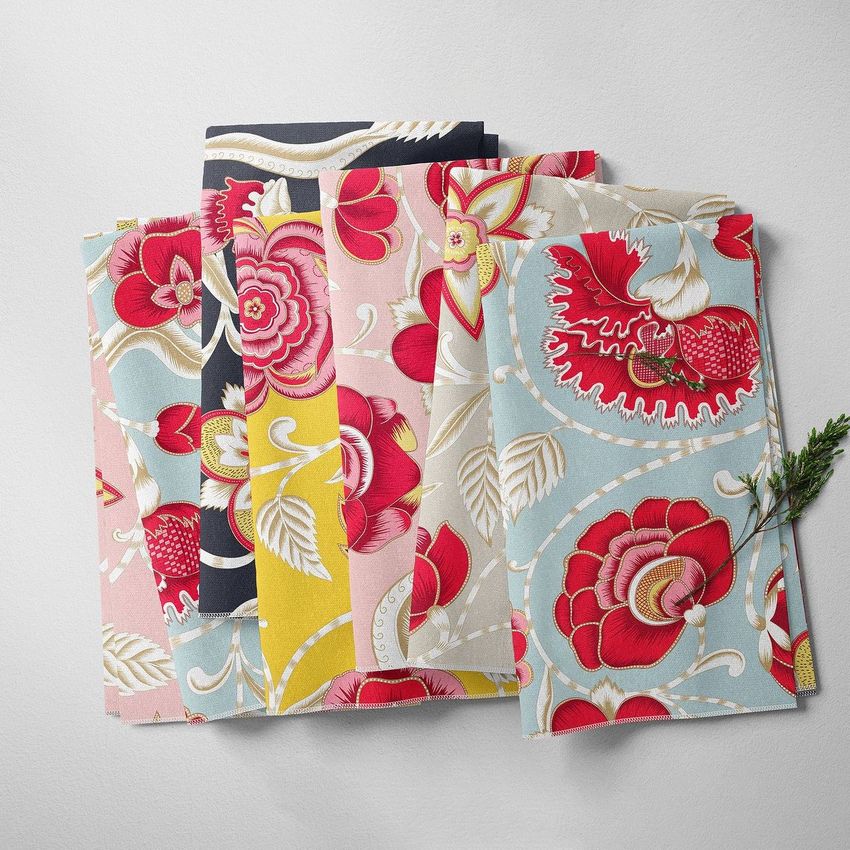 Folded fabrics mockup featuring multiple fabric pieces with bold floral patterns in red, pink, yellow, and blue on a light surface.