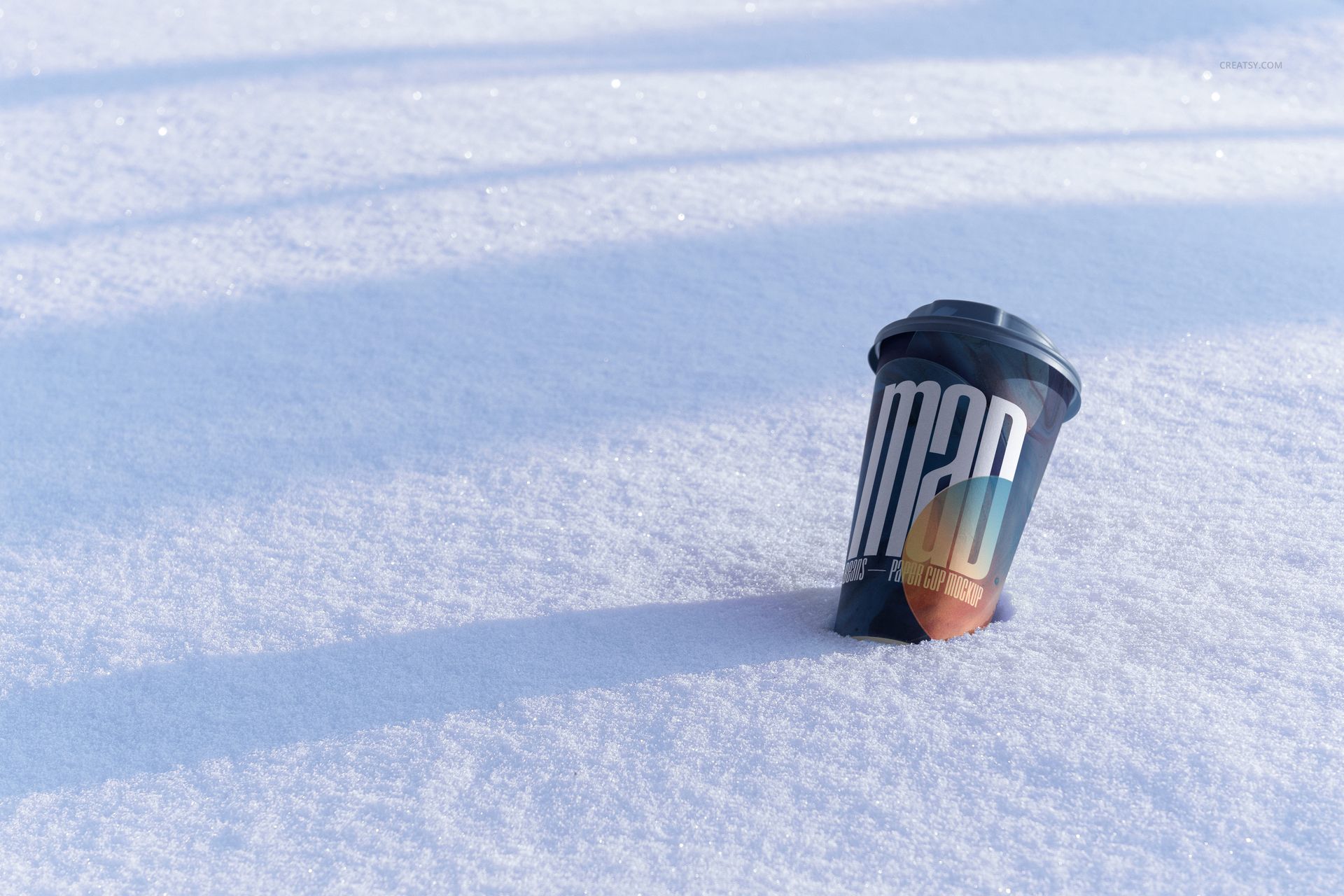 Winter-themed PSD mockup featuring a paper cup with a black lid and bold text design resting on snowy ground.