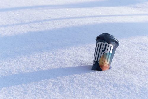 Winter-themed PSD mockup featuring a paper cup with a black lid and bold text design resting on snowy ground.