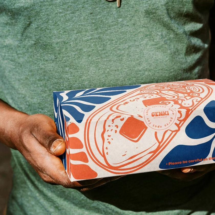 Person holding a takeaway box mockup with bold blue and orange abstract patterns and food illustrations on a neutral background.