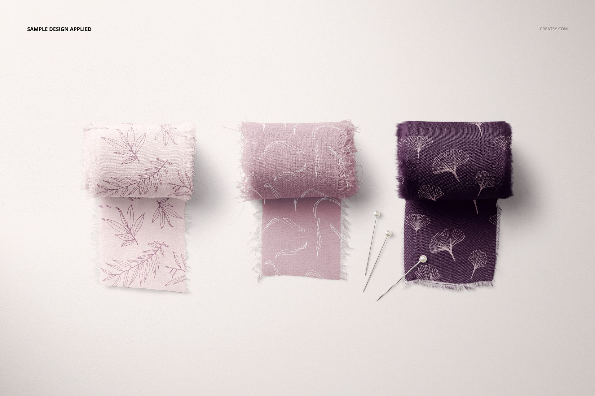 Pins and Silk Ribbons Mockup showing three rolled ribbons in muted pink and purple hues, each with fine line botanical prints, arranged on a neutral background.