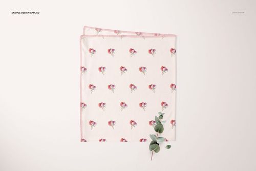 Swaddle blanket mockup featuring a repeating red and purple flower design, shown flat with a sprig of greenery.