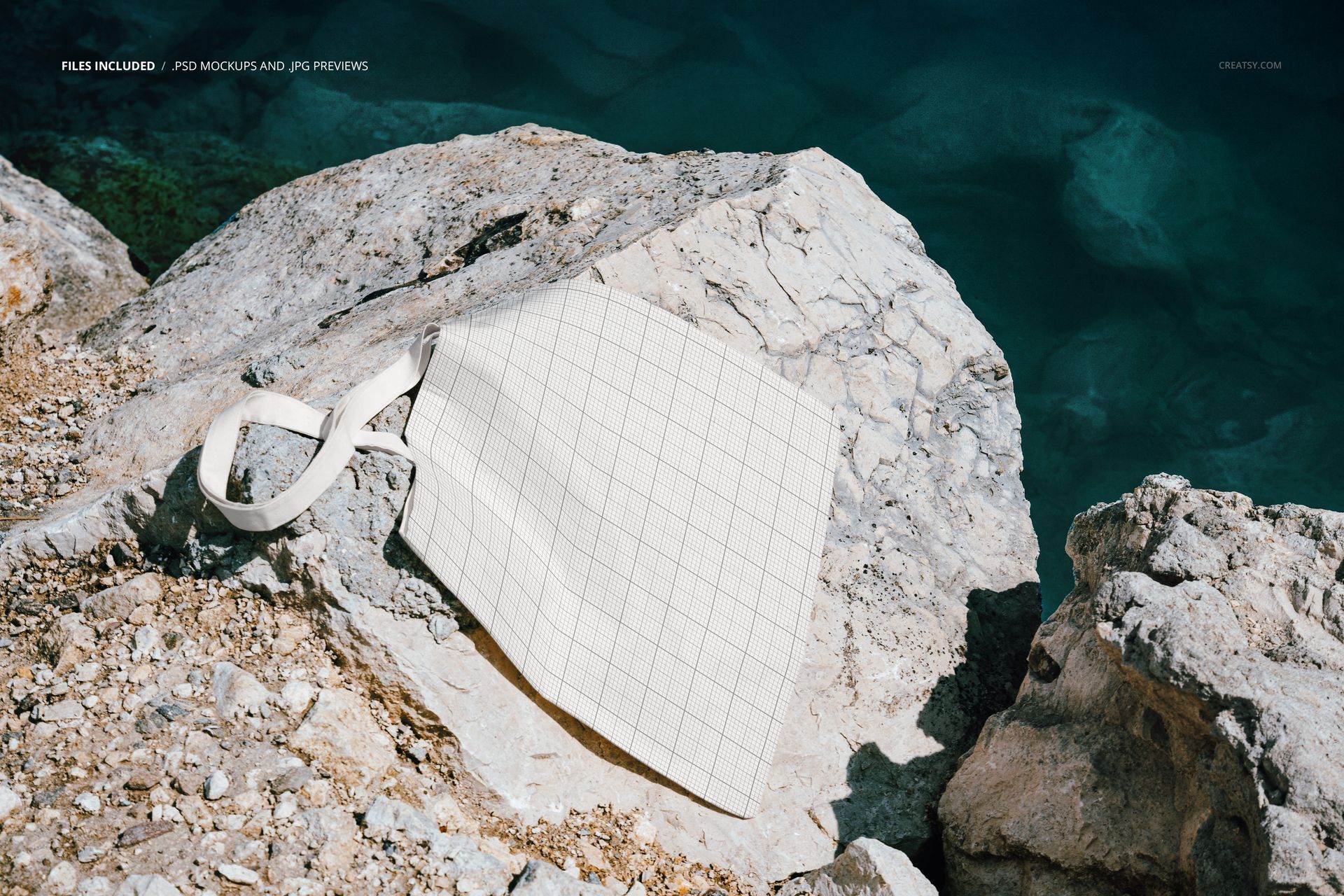 Canvas tote bag with a grid pattern lying on sunlit rocky sea cliffs above deep blue water, front view mockup.