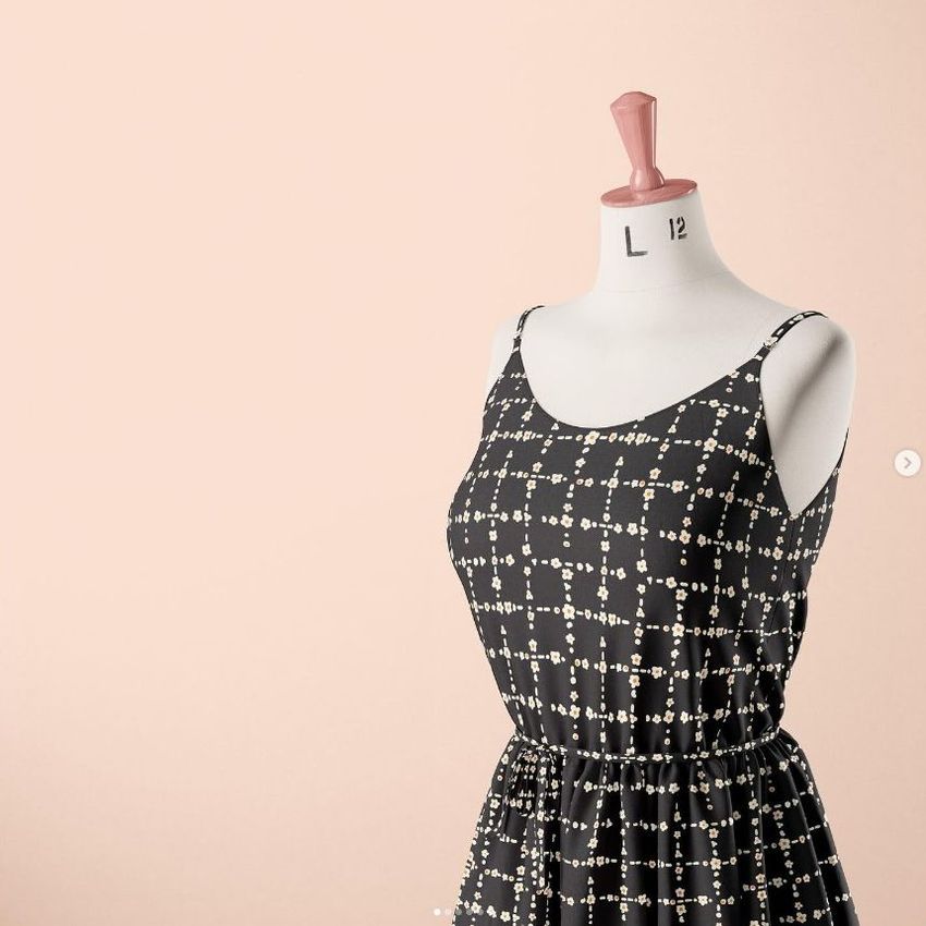 Fabric dress mockup featuring a sleeveless black dress with a ditsy floral pattern on a mannequin against a pale peach background.