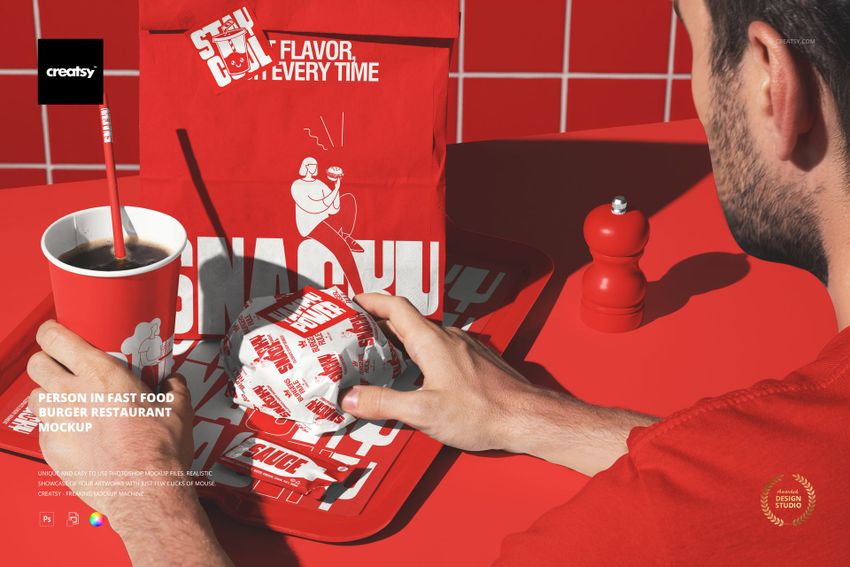 Front view of a person holding a wrapped burger at a red fast food restaurant table with drink and packaging mockup.