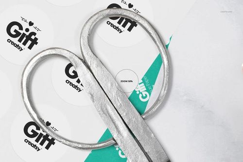 Close-up view of silver scissors on white tissue paper with circular gift stickers and teal wrapping paper in a mockup scene.