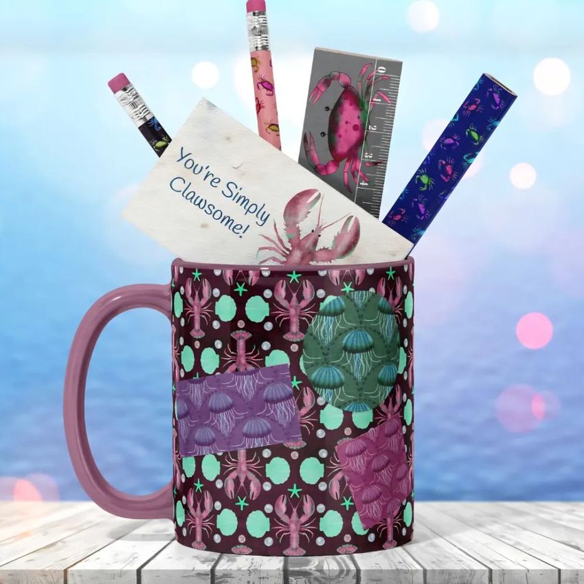 Mug mockup featuring a pink and teal crab pattern, filled with office supplies like pencils, a ruler, and a note card on a wooden surface.