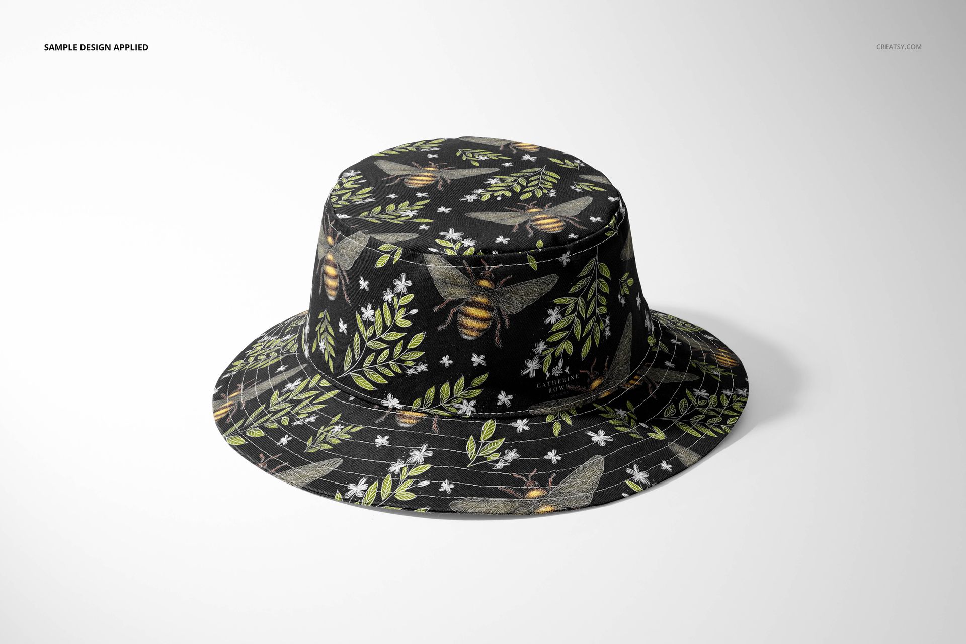 Adult bucket hat mockup displaying a dark fabric decorated with botanical and bee patterns, presented on a white surface.