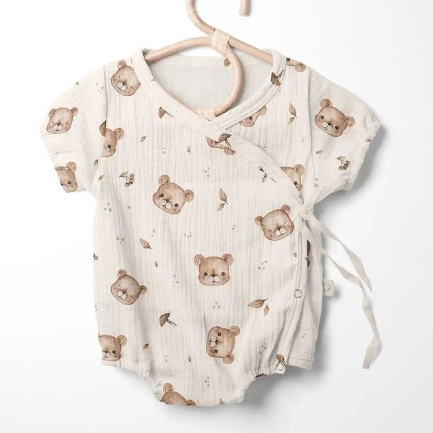 Muslin onesie mockup featuring a short-sleeve baby bodysuit with a teddy bear pattern, displayed on a wooden hanger.