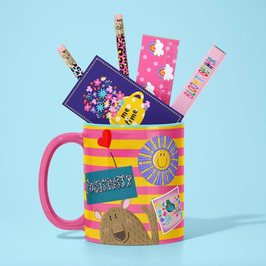 Mug mockup with pink handle and yellow stripes, filled with colorful stationery items like pencils, rulers, and cards on a blue background.