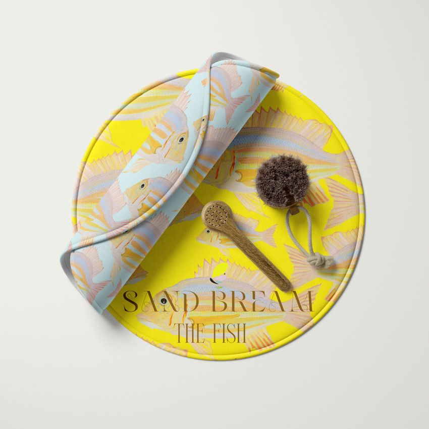 Round polyester bath mat mockup with a yellow fish pattern, rolled towel, wooden brush, and bath sponge on a white background.