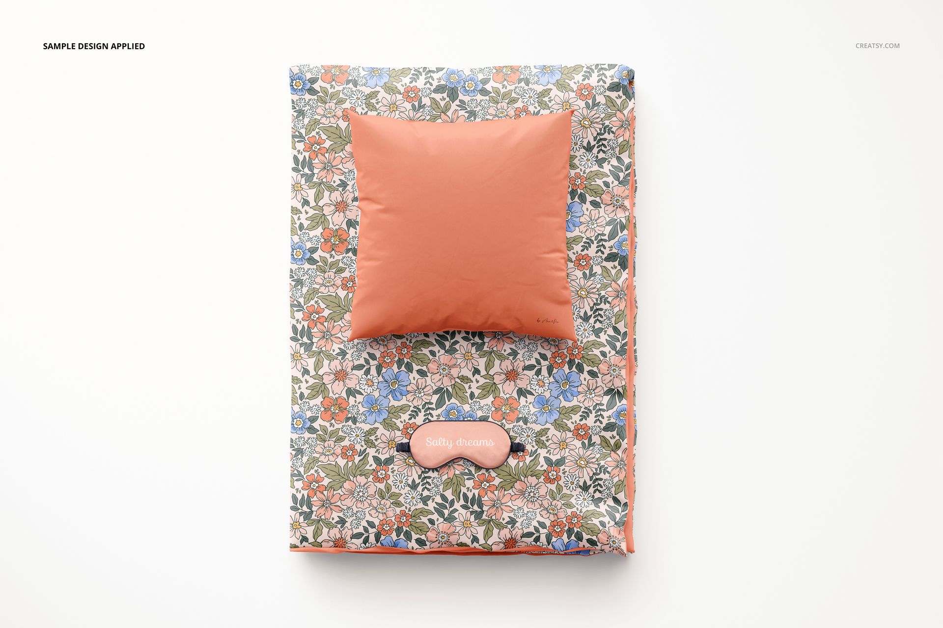 PSD mockup showing a folded duvet with multicolored flowers and a coral pillow, arranged on a clean white backdrop.
