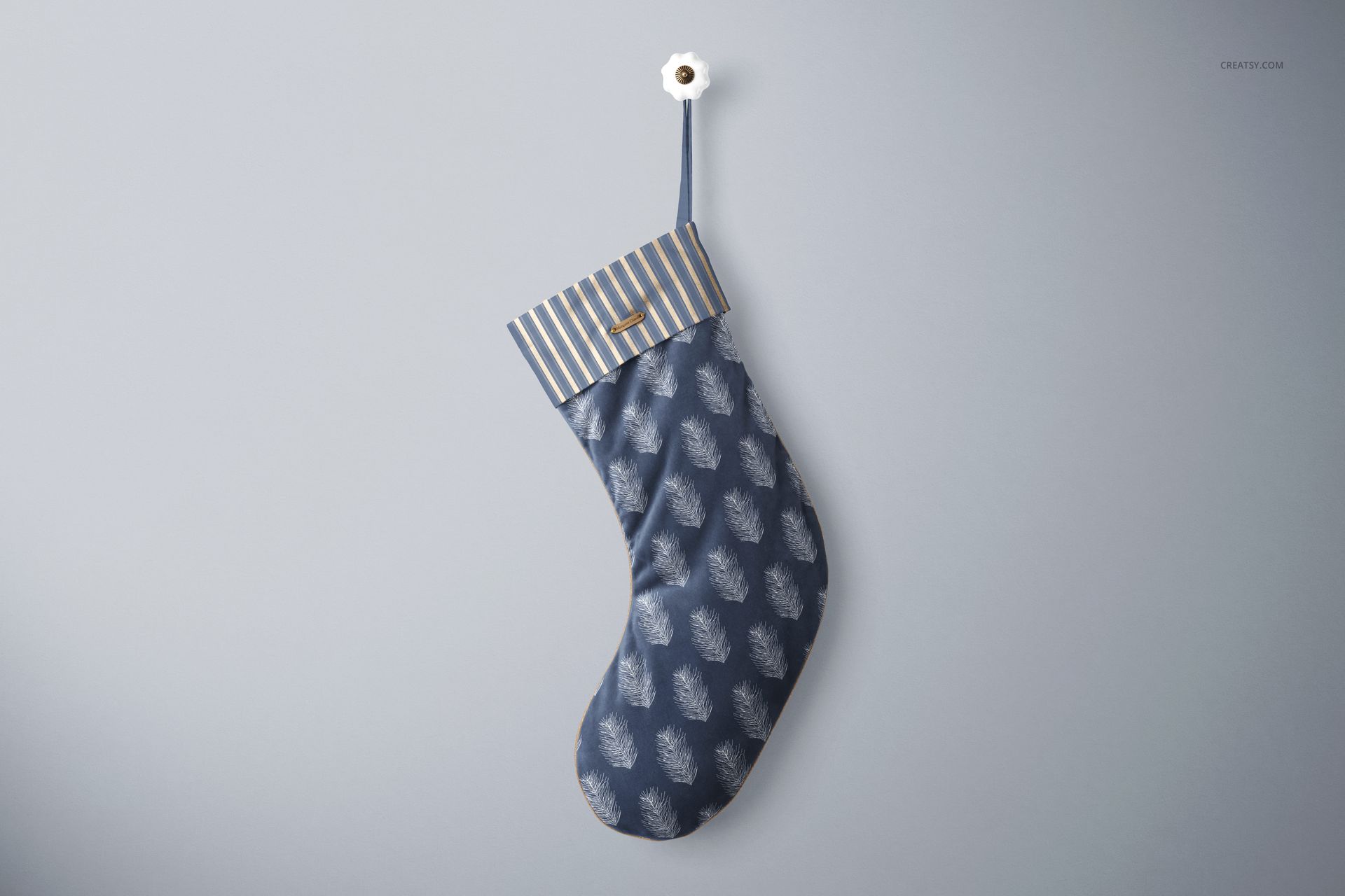 Single velvet Christmas stocking mockup with blue and white feather motif, striped cuff, and gold accent, against a gray wall.