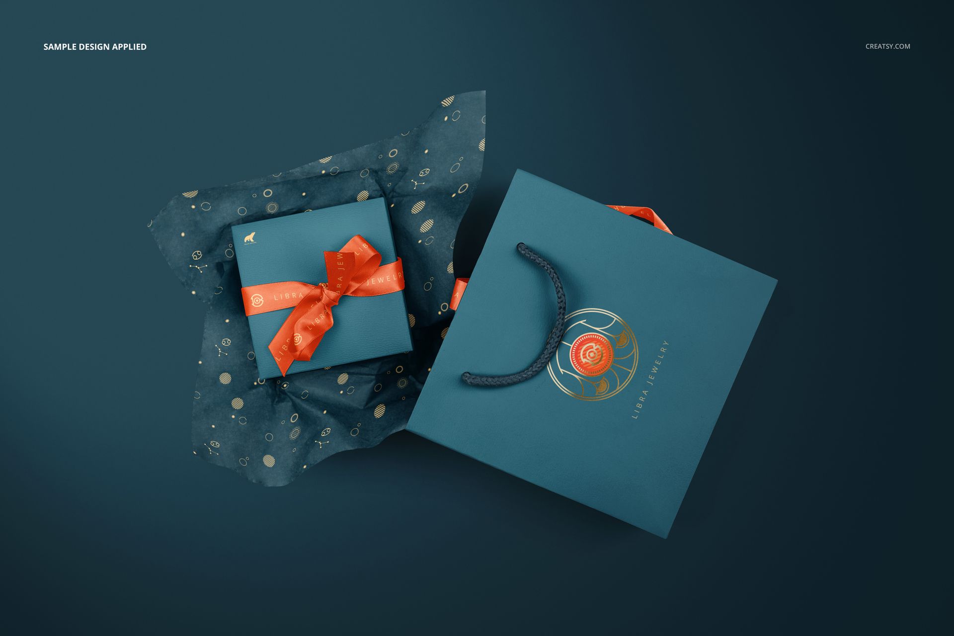 Jewelry box and gift bag mockup set in blue tones, with polka dot tissue paper and orange ribbon, arranged on a dark background.